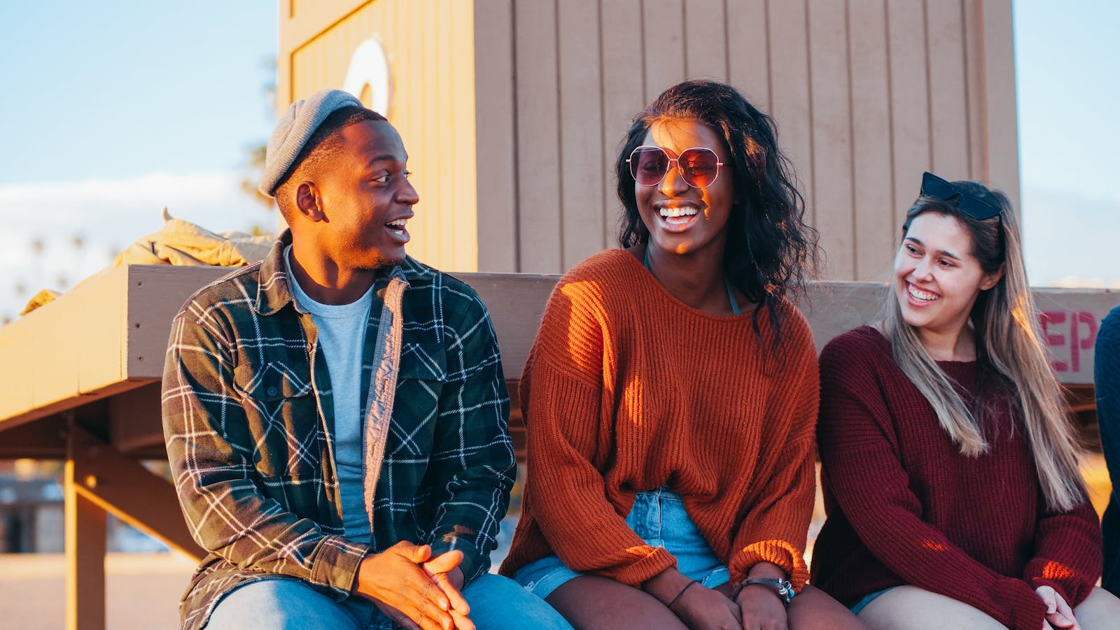 Three diverse friends laughing together outdoors in warm golden-hour light.